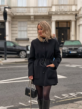 a lady wears a black wool coat with black tights and boots
